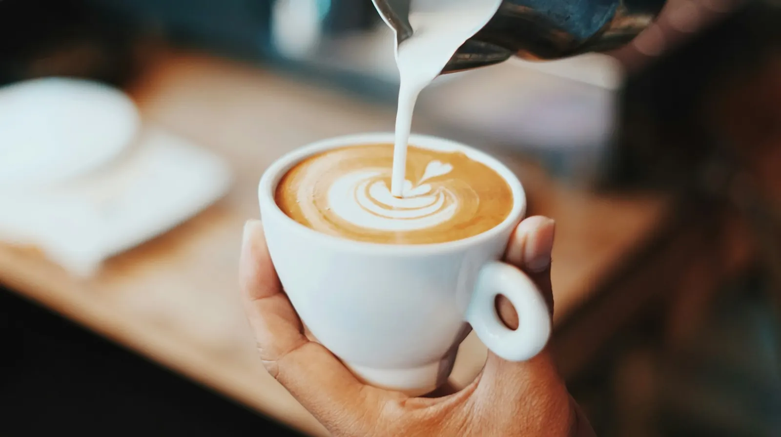 Milchschaum wird in einen Cappuccino gegossen